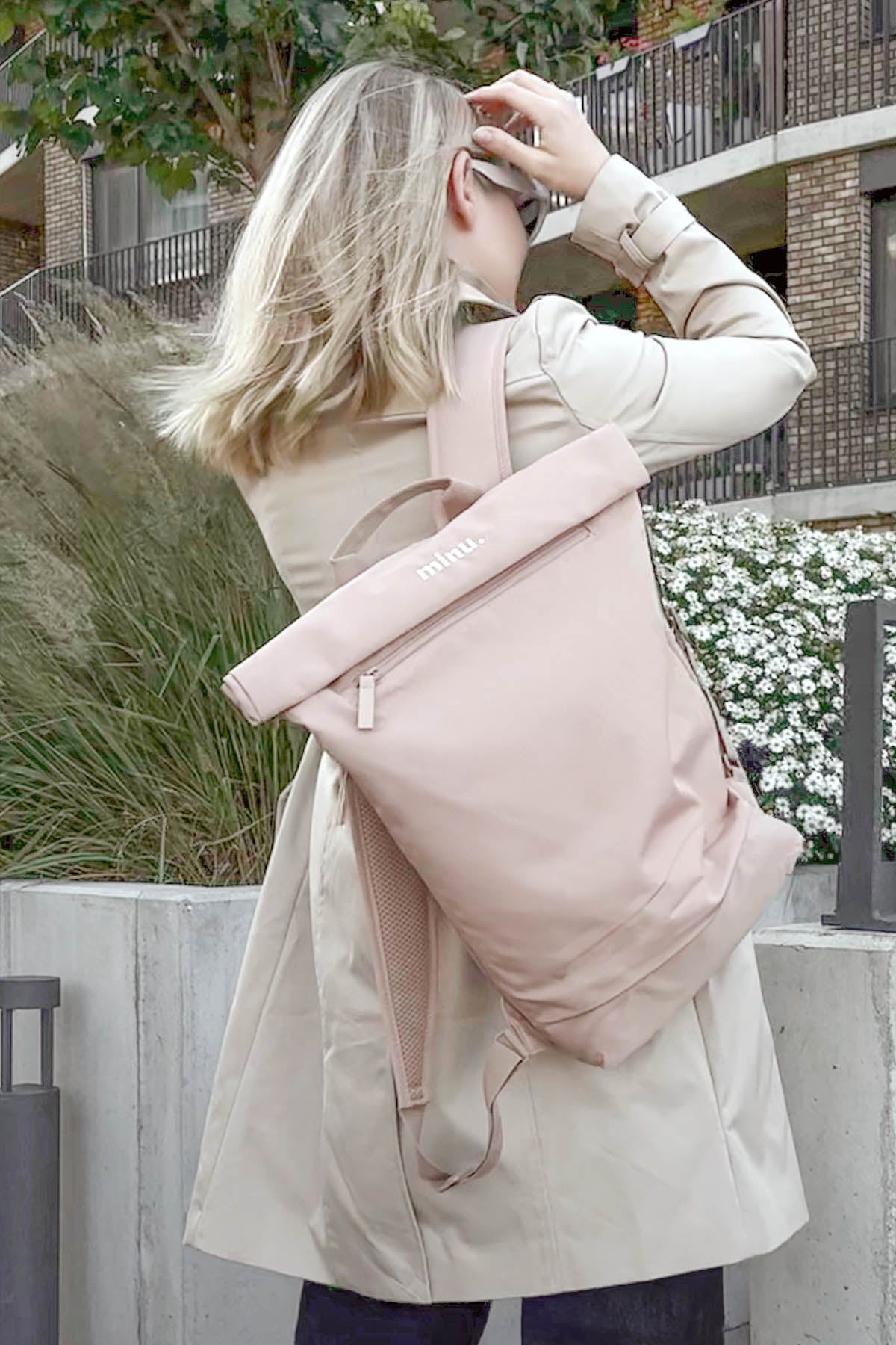 Person wearing a beige coat with a pink backpack outdoors.