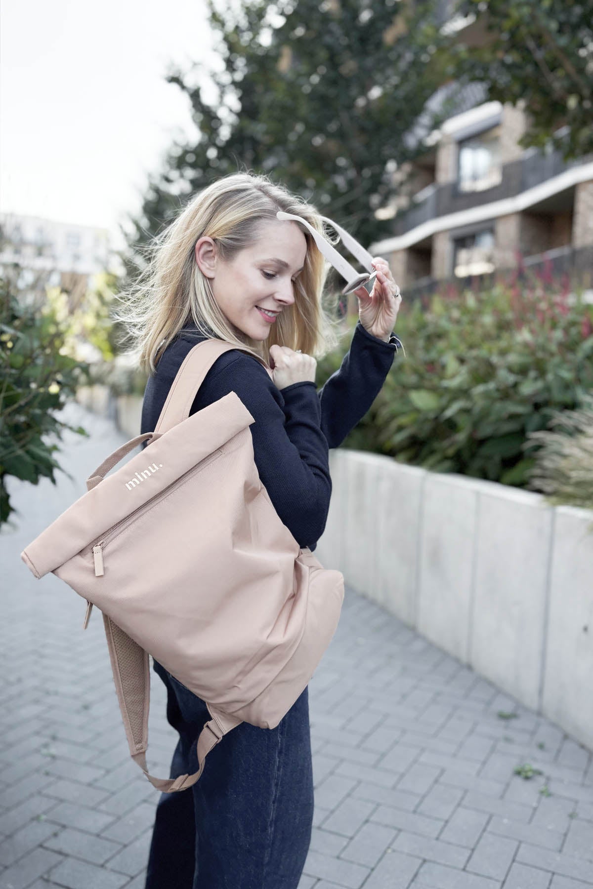 Woman holding a beige backpack outdoors on a sidewalk