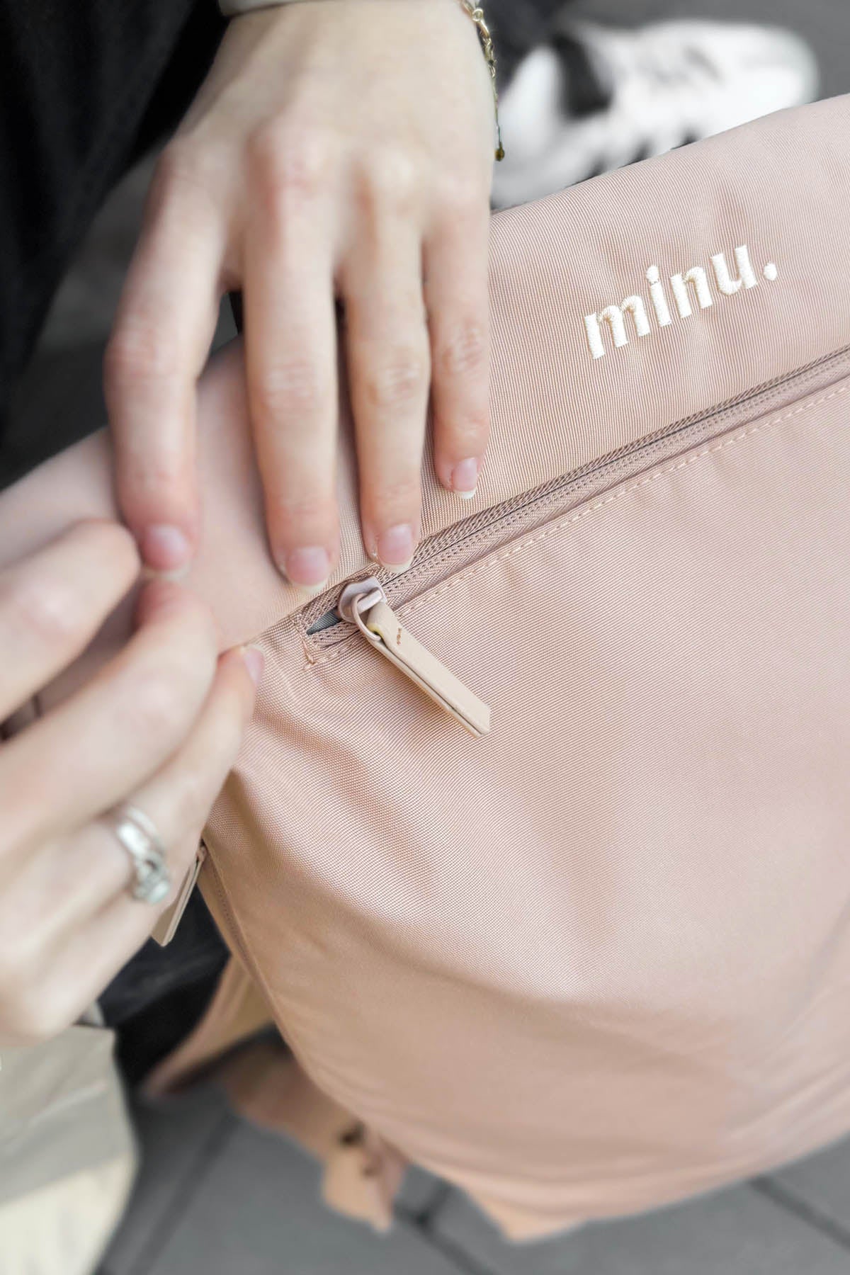 Close-up of a hand opening a blush pink bag with 'minu.' branding.